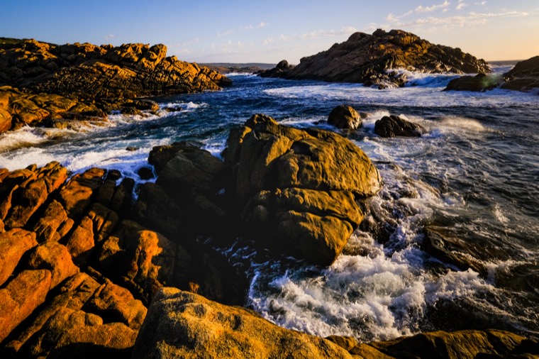 Surf breaking over golden rocks at sunset, Western Australia
